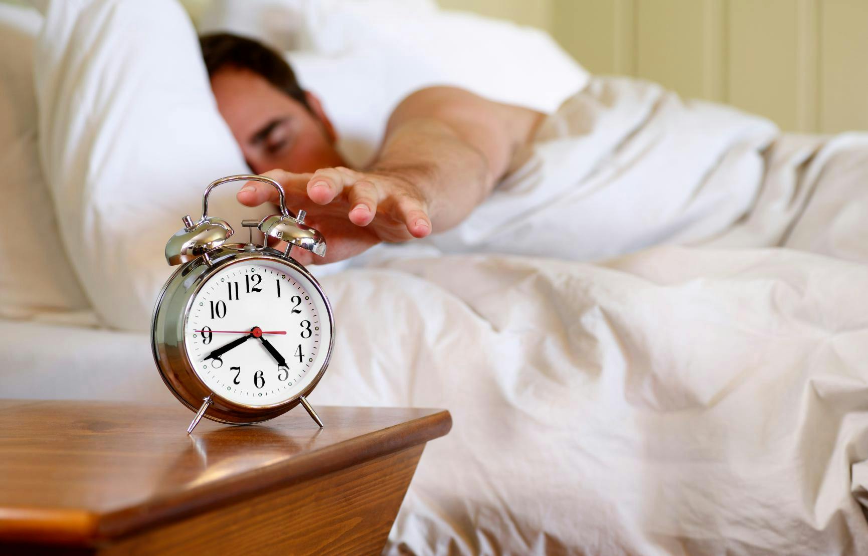 Man reaching to hit snooze on his alarm clock.