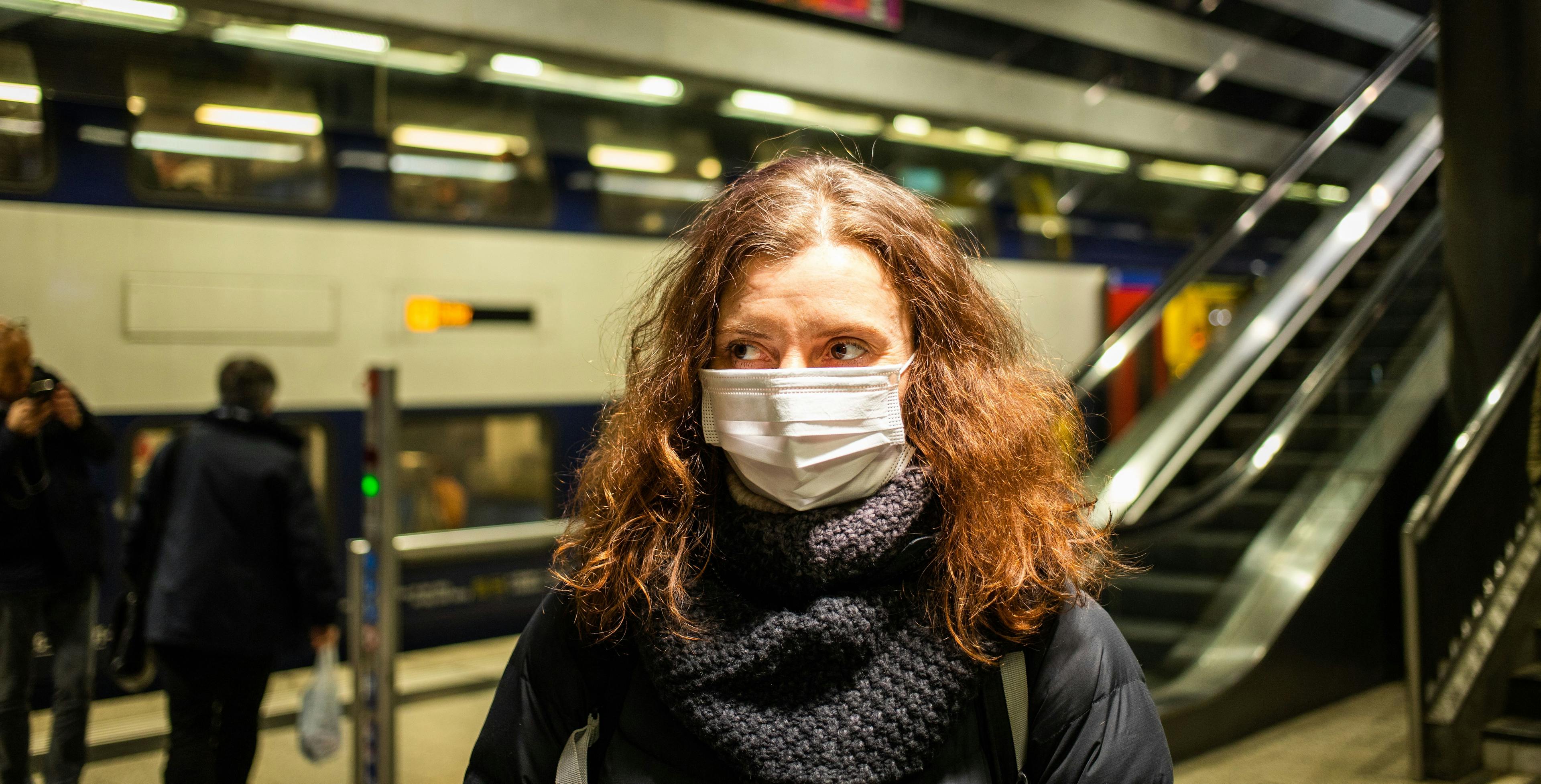 A woman wearing a mask at a train station.