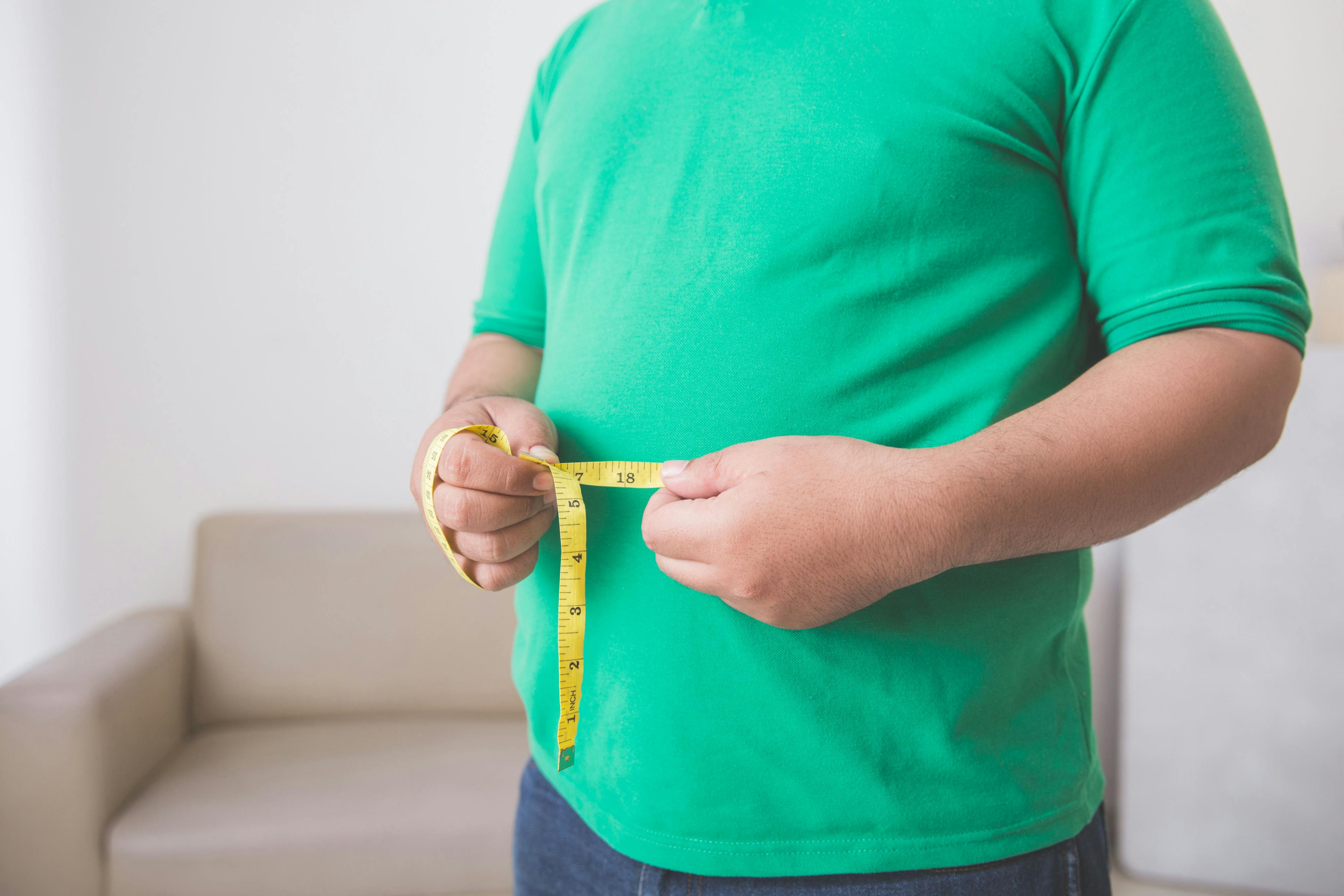 A person with overweight/obesity measuring their midsection.