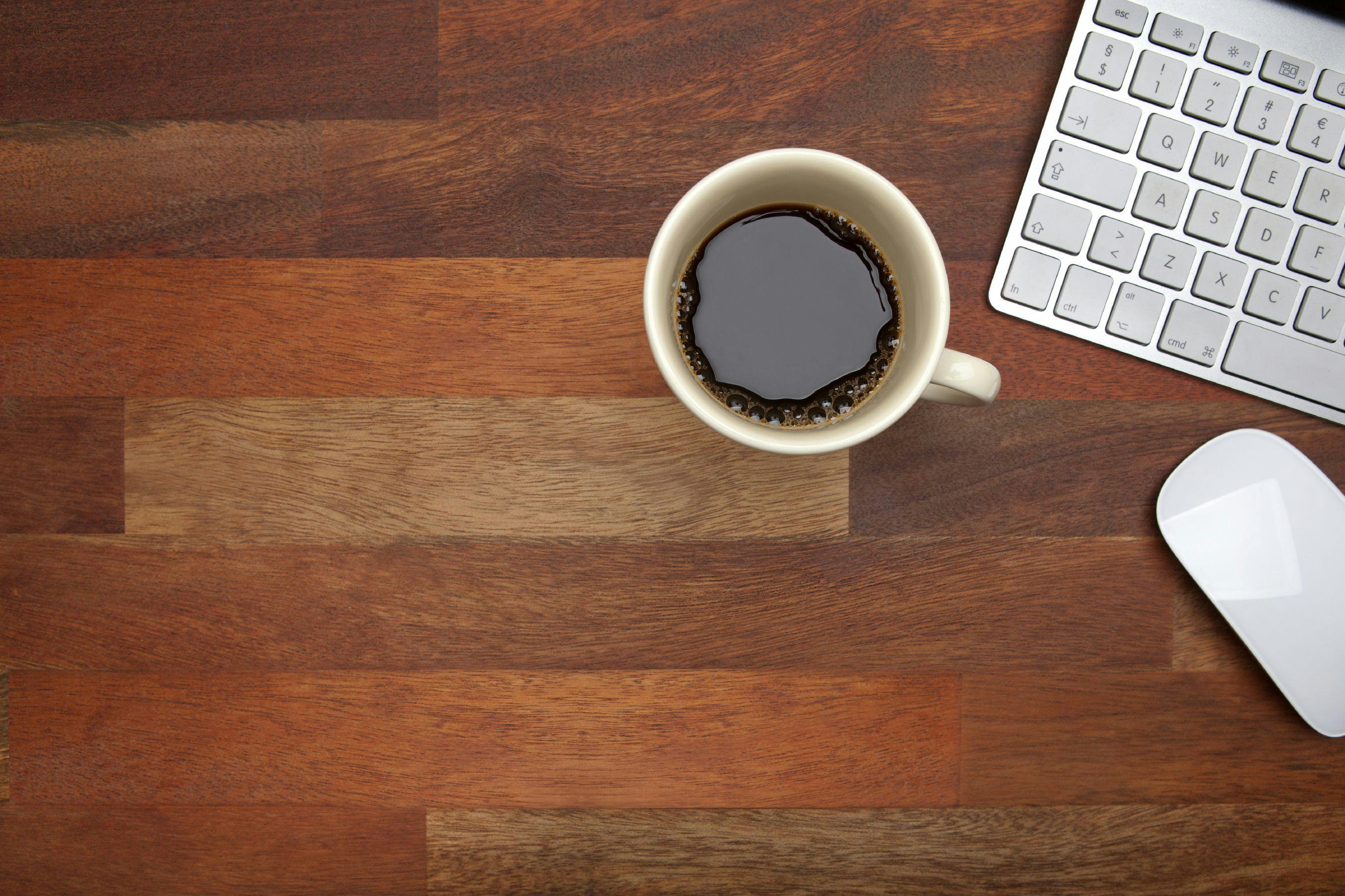 Stock image showing a cup of coffee next to a laptop keyboard.