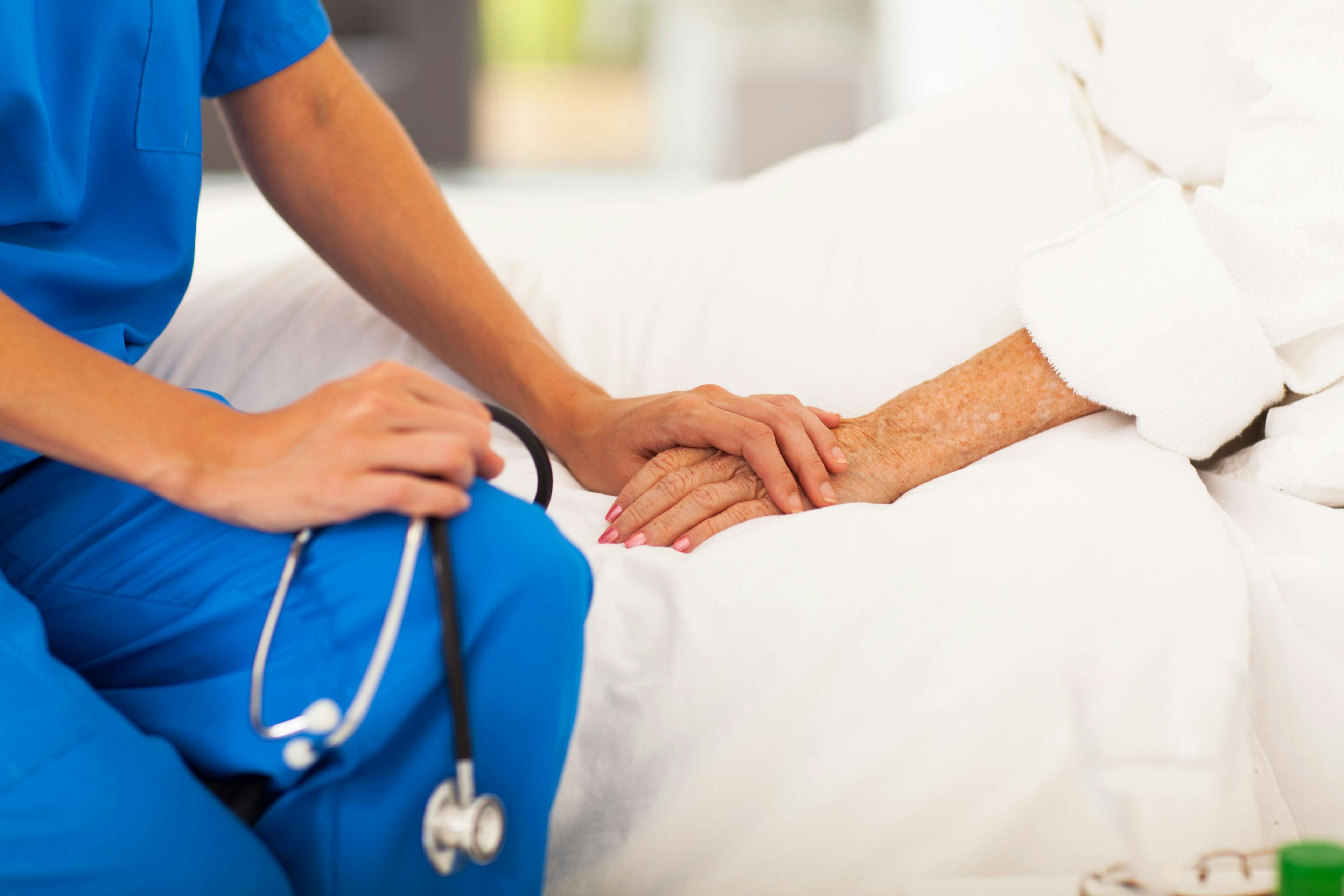 A close-up photo of a care provider holding the hand of an older person in the hospital.