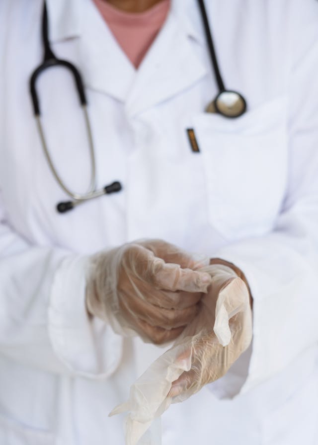 Doctor wearing a white coat putting on gloves to prepare for procedure | Credit: Pexels