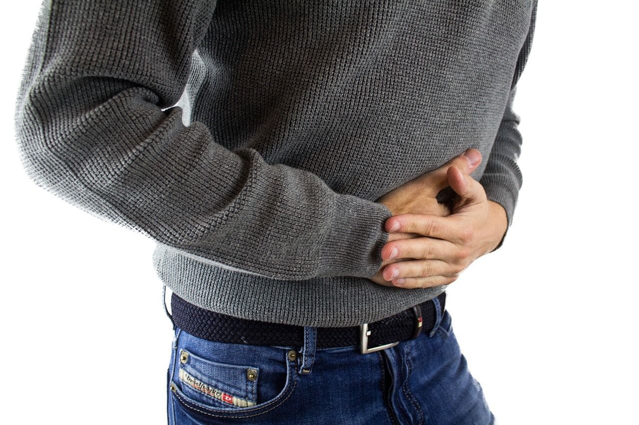 Man wearing gray sweater and jeans holding stomach in pain